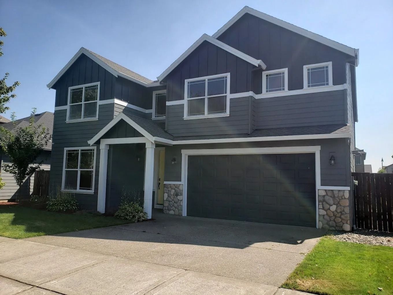 Two-story house with dark gray vertical and horizontal siding, a large garage, and stone accents on a sunny day.