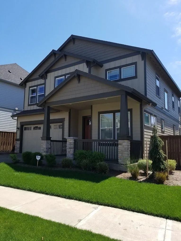 A two-story suburban house with beige siding, dark brown trim, a stone-accented front porch, and an attached garage.