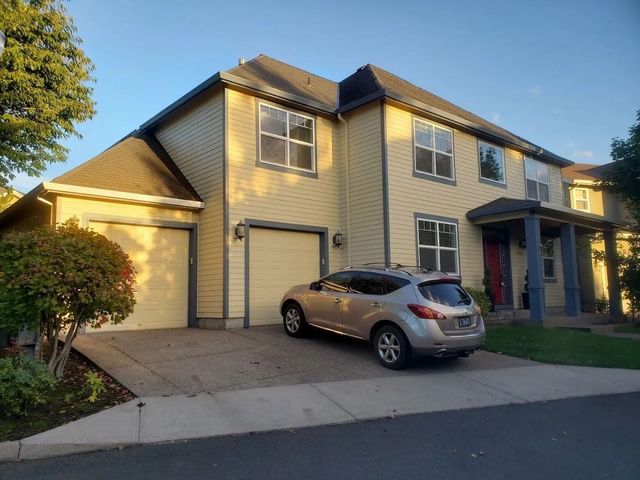 A two-story, yellow-sided house with a dual garage and a silver SUV parked in the driveway on a sunny day.