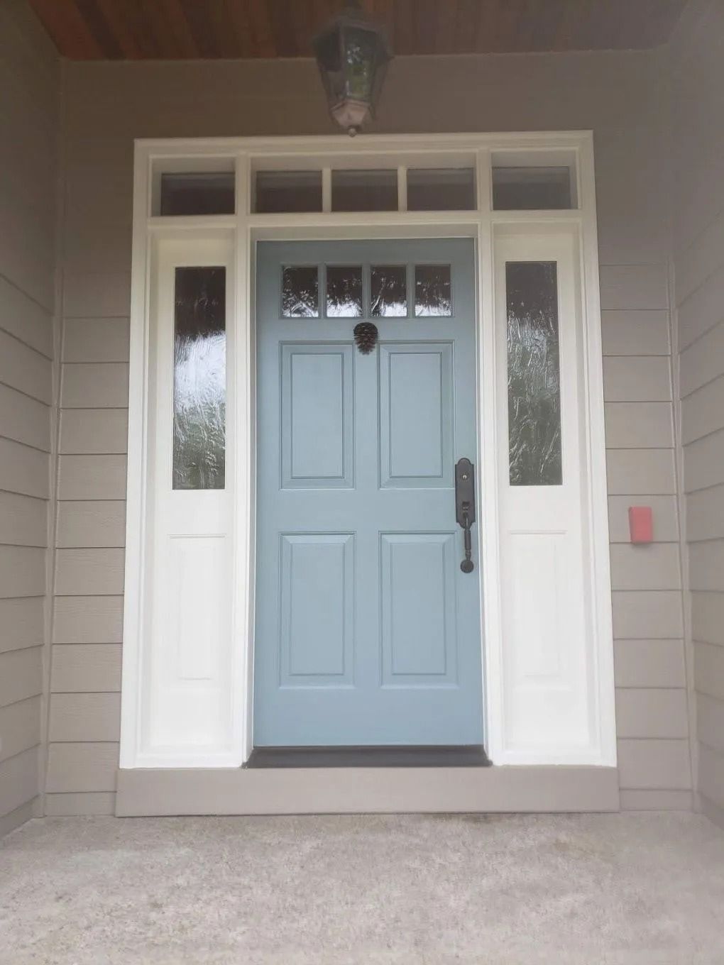 A light blue, four-panel front door with a black handle and knocker, framed by white side lights and a transom window.