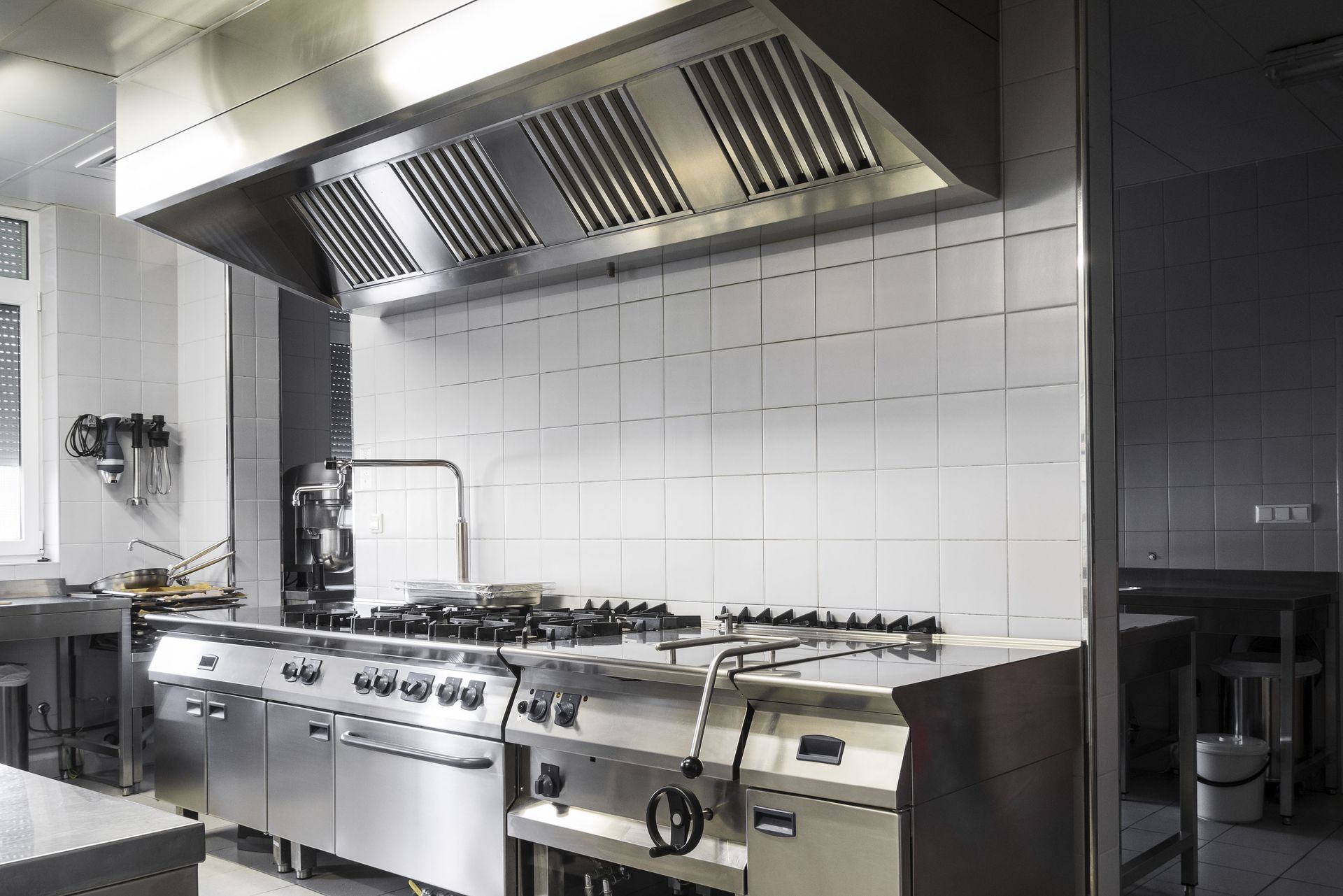 Commercial kitchen with stainless steel stove, range hood, and tiled wall.
