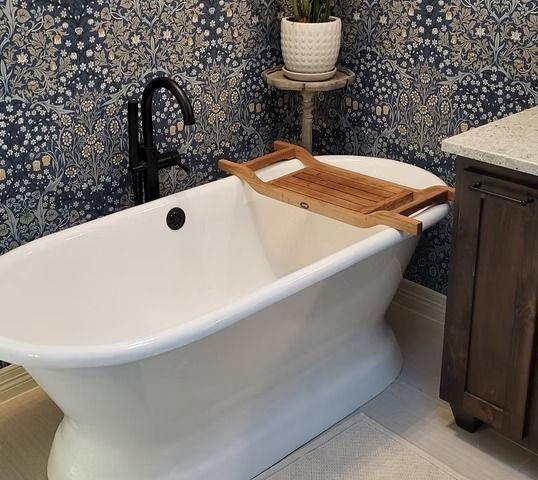 White freestanding bathtub with wooden bath tray, next to a dark wood vanity.