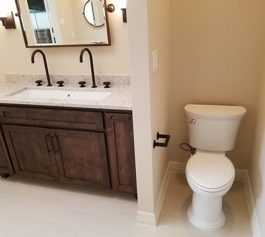 Bathroom with dark brown vanity, white sink, and toilet in a separate alcove, with light tan walls.