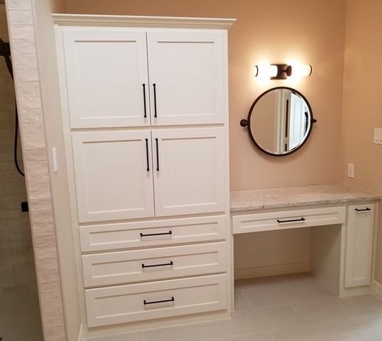 White cabinet and vanity in a bathroom with a round mirror.