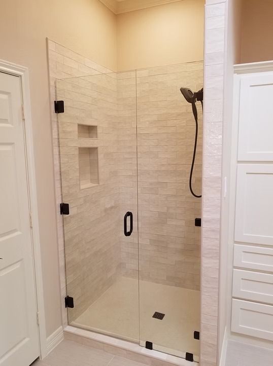 Glass shower enclosure with black hardware and beige tiled walls.