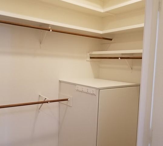 Empty, white closet with built-in shelves and rods. Wooden rods contrast with white walls.