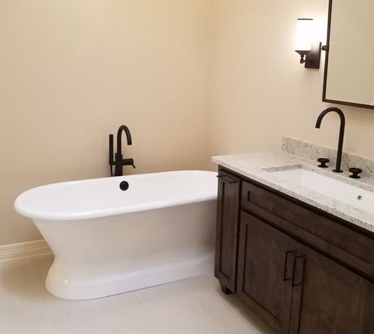 Bathroom with a white freestanding bathtub and dark-colored fixtures next to a vanity with a white countertop.