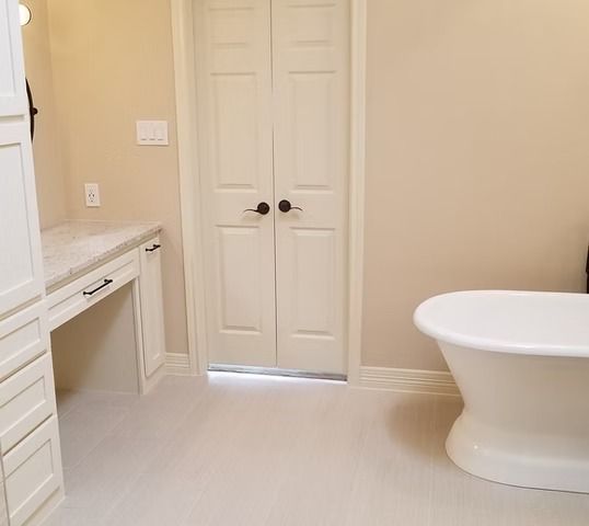 Bathroom with white freestanding tub, vanity, and double doors; light walls and floor.