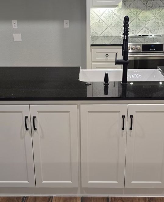White kitchen cabinets with black countertop, black faucet, and patterned backsplash.