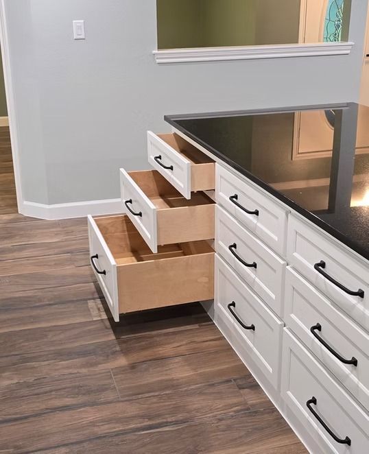 White kitchen drawers, some open, built into a countertop with a dark surface.
