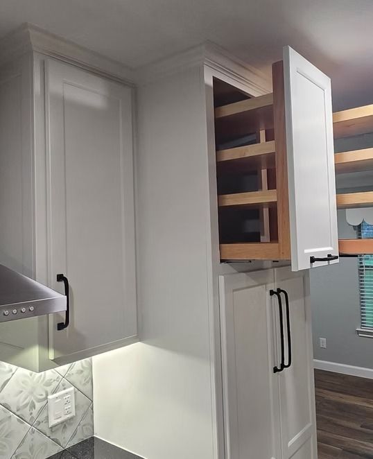 White kitchen cabinets with pull-out shelving, one door open. Black handles, light above counter.