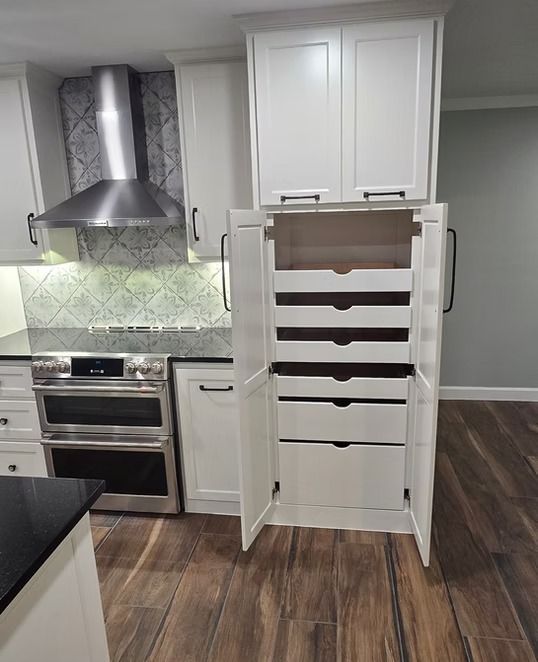 White kitchen cabinet with pull-out drawers, next to a stove and range hood. Dark wood floor.