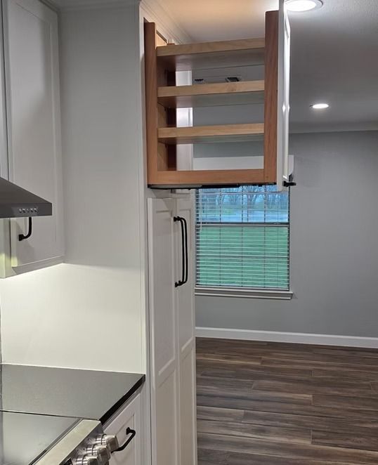 Pull-out spice rack inside a white kitchen cabinet. Light brown shelves, black cabinet handle.