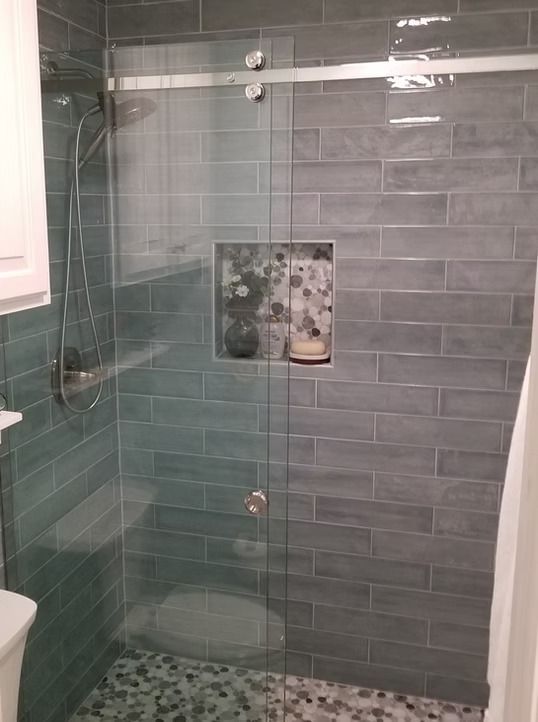 Gray tiled shower with glass door and built-in shelf; gray, blue, and white tones.