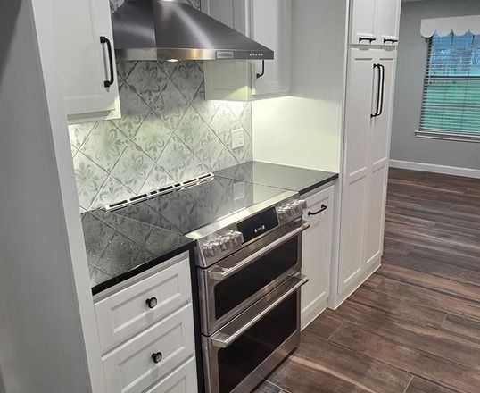 Modern kitchen with white cabinets, stainless steel oven, backsplash, and hood.