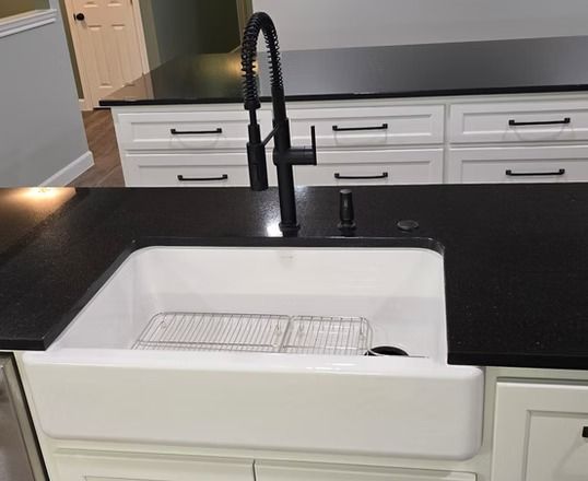 White farmhouse sink with black faucet on black countertop.