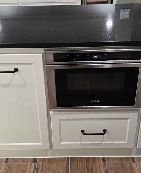 Built-in stainless steel Bosch microwave and a white cabinet with a drawer beneath a black countertop.