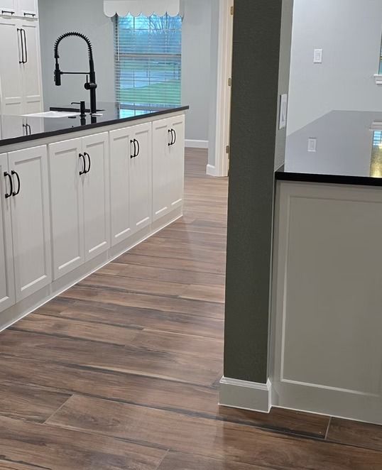 Kitchen interior with white cabinets, black countertops, and wood-look flooring. Black faucet and hardware.
