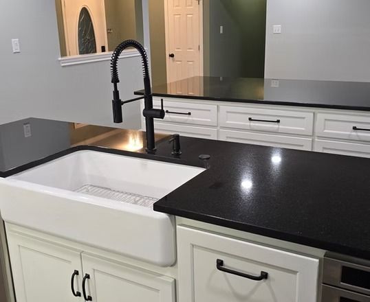 Kitchen island with black countertop, white farmhouse sink, and black faucet against white cabinets.