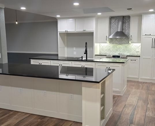 Modern kitchen with white cabinets, black countertops, and wooden floors.