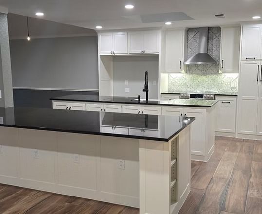 Modern kitchen with white cabinets, dark countertops, and hardwood floors.
