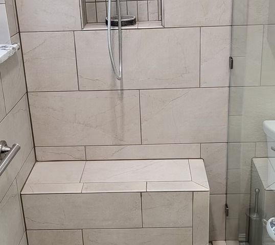 Tiled shower with built-in bench, shower head, and glass door. Light beige tiles throughout.
