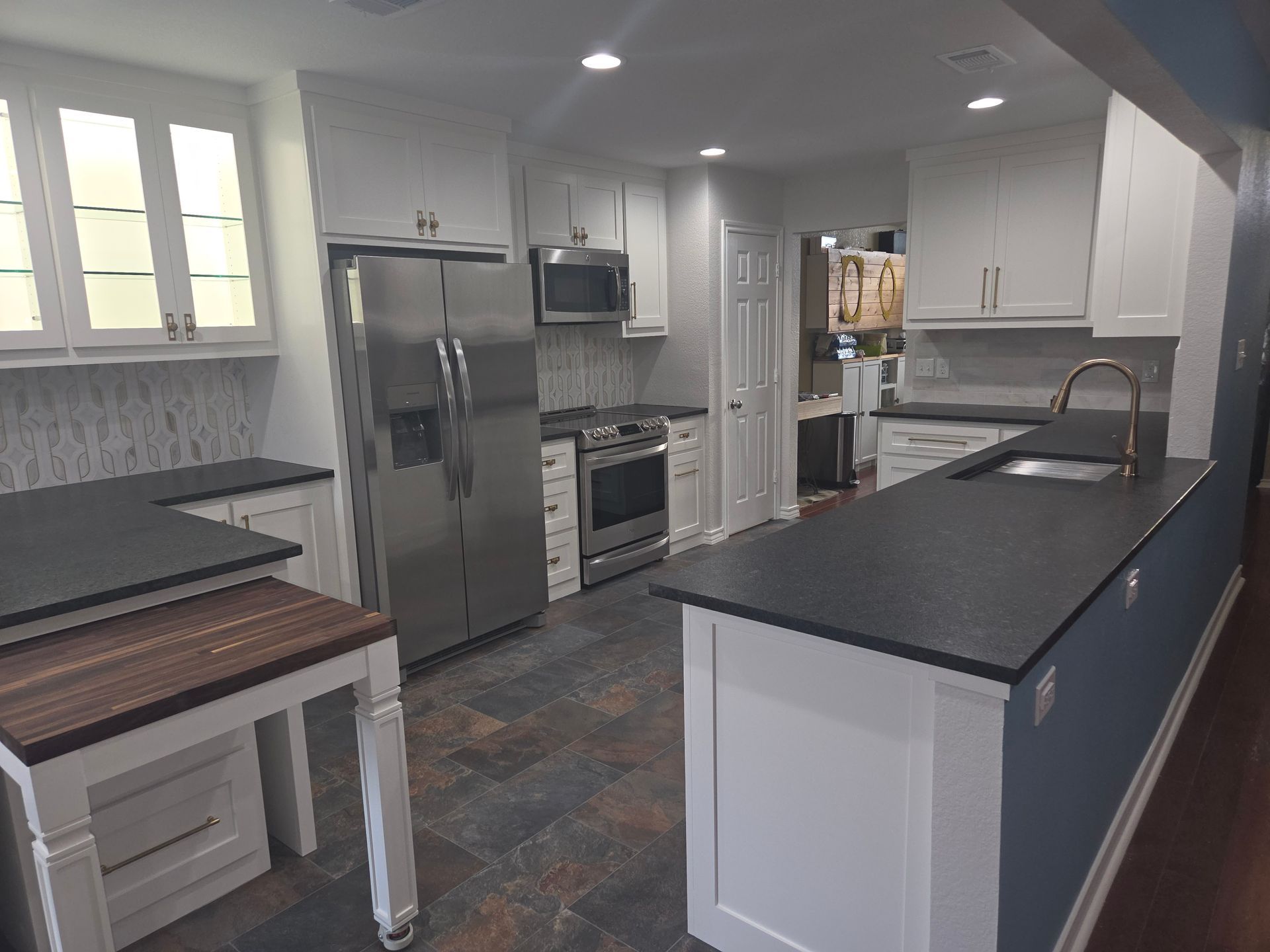 A modern kitchen with white cabinets, dark countertops, a stainless steel refrigerator, and slate-style flooring.