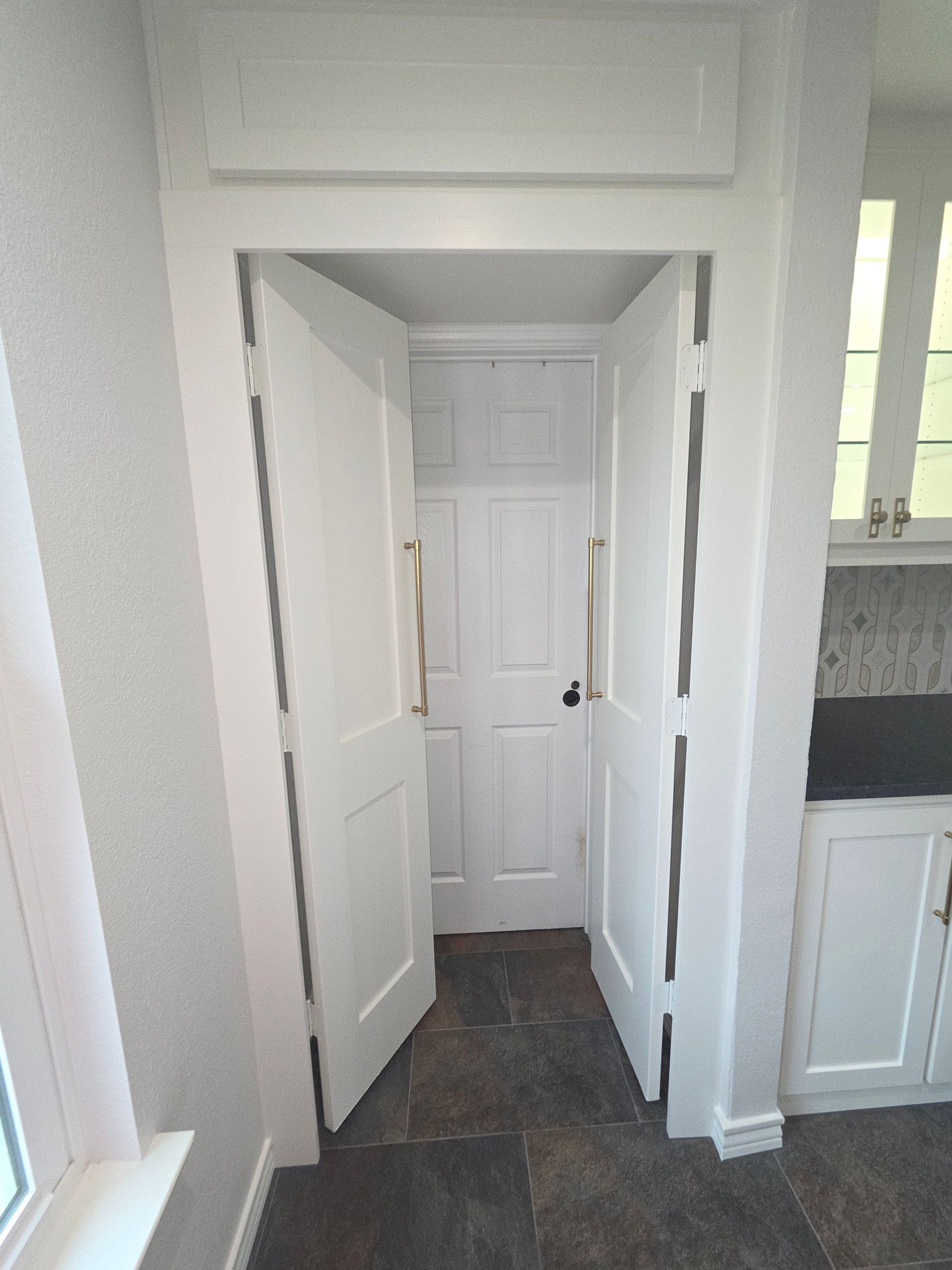 A doorway with white paneled double doors leading into a small room, where a white single door is visible in the background.