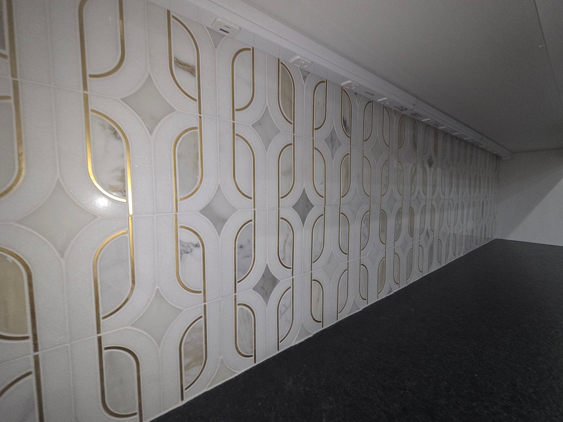 A wall with a repeating geometric pattern of white marble tiles accented by thin, vertical brass or gold metal strips.