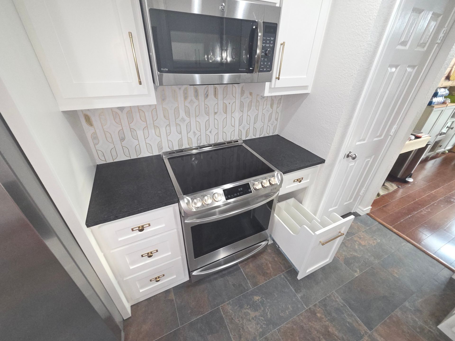 A kitchen area with white cabinets, a black countertop, a stainless steel oven and microwave, and tiled flooring.