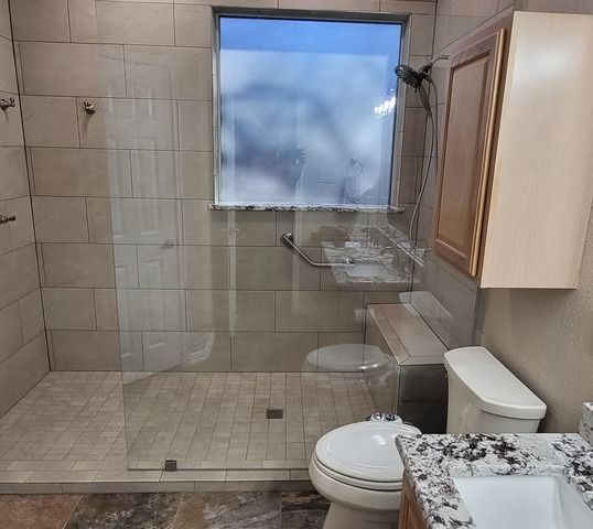 Bathroom with a clear glass shower, toilet, and vanity with a light countertop.