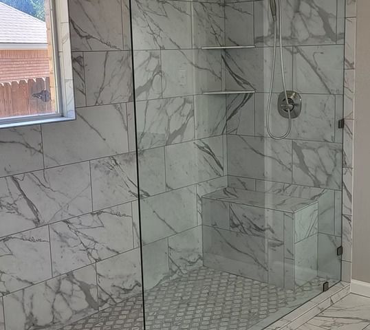 Glass shower with marble-look tiles, a built-in bench, and shelves. Light, modern bathroom.