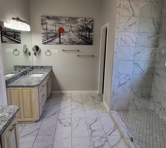 Bathroom with marble tile floor and walls, light wood vanity, art, and glass shower.