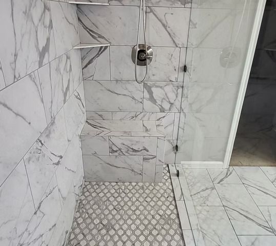 Shower with marble-look tile, glass door, and mosaic floor.