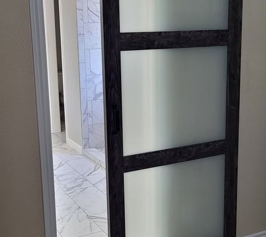 Sliding interior door with frosted glass panels, dark wood frame, open to bathroom with marble floor.