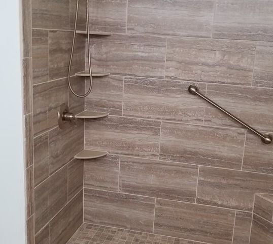 Shower with brown tile, built-in shelves, and a grab bar for accessibility.