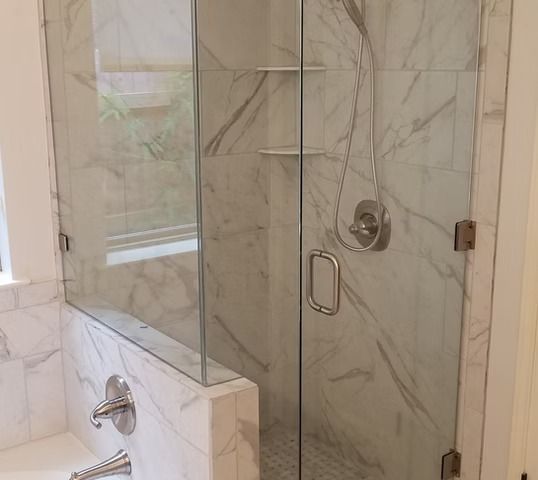 Glass shower enclosure with white marble tiles.