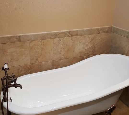 White clawfoot bathtub against tiled wall, with bronze faucet fixture.