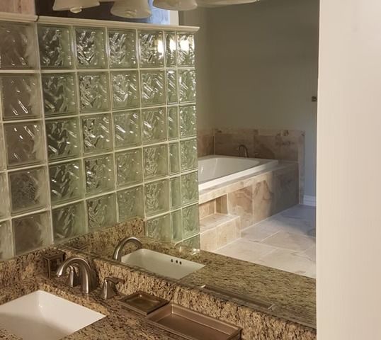 Bathroom with granite countertop and a glass block wall separating the vanity area from a bathtub.