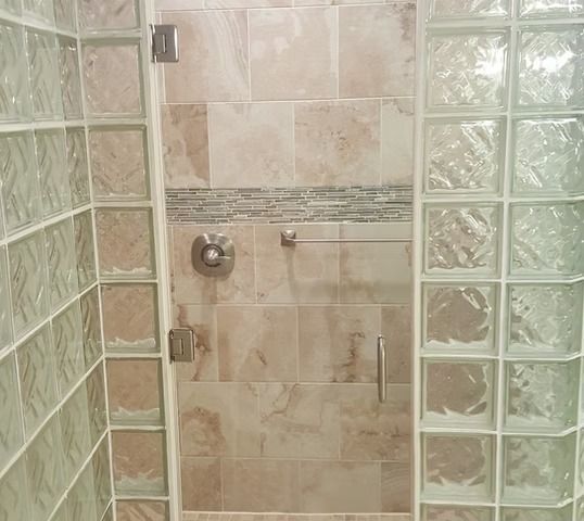 Shower stall with glass blocks on sides, beige tiled walls, and a glass door.