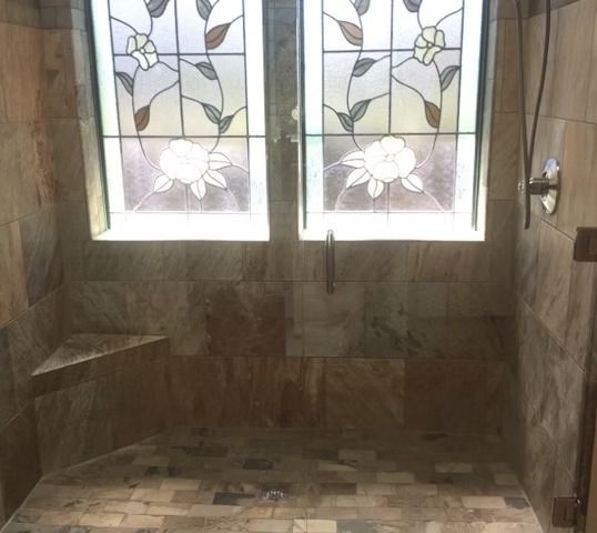 Shower with stained glass windows, stone tile walls and floor, and corner seat.