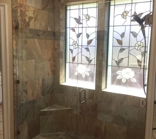 Shower with stone tile walls, glass door, and stained glass window with floral design.