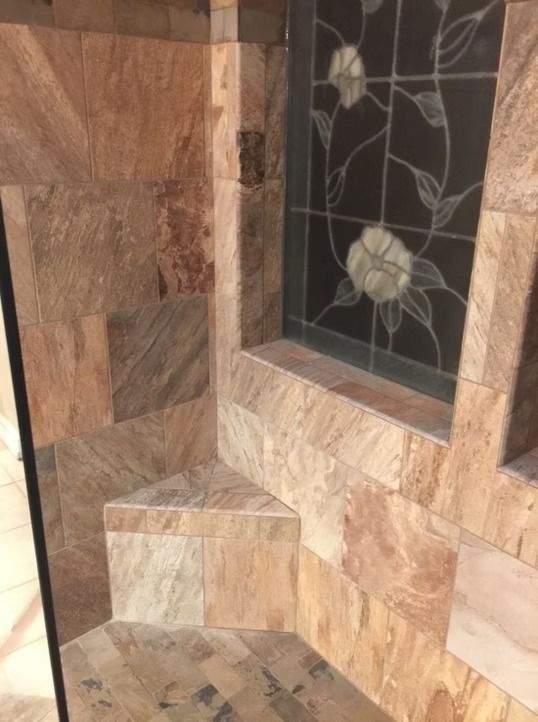 Tiled shower corner with a built-in triangular bench. A stained glass window sits above the bench.