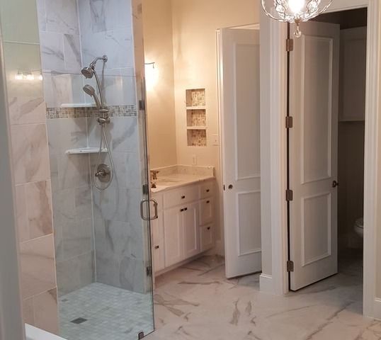 Bathroom with marble tile shower, white vanity, two doors.