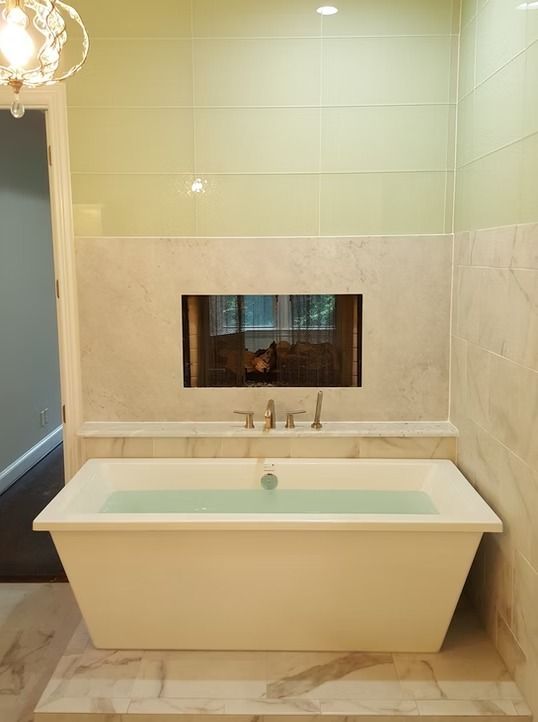 White bathtub with water, built into tiled wall with a recessed TV, in a bathroom.