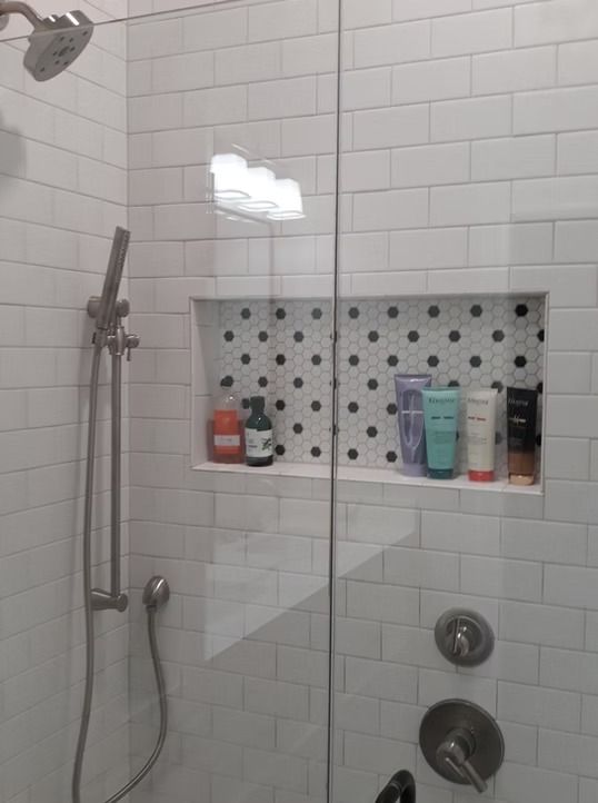 Shower with white subway tile, a glass door, and a built-in shelf with toiletries.