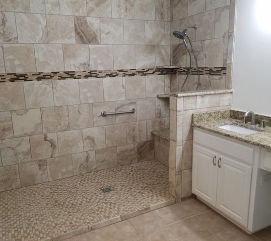Accessible shower with pebble floor, beige tile walls, grab bar, and vanity.