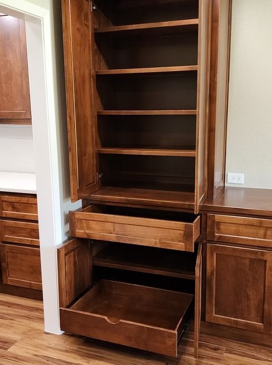 Wooden pantry cabinet with open shelves and pull-out drawers in a kitchen.