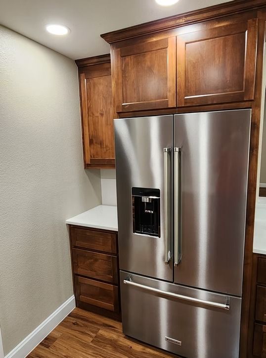 Kitchen with a stainless steel refrigerator, wooden cabinets, and white countertops.
