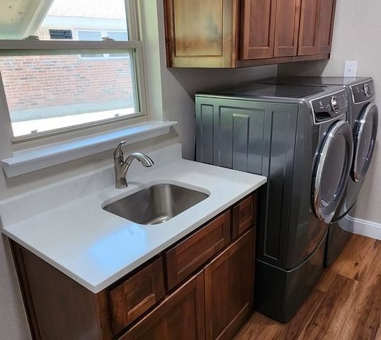 Laundry room with sink, cabinets, washer, dryer, and a window. Brown wood cabinets and white countertop.